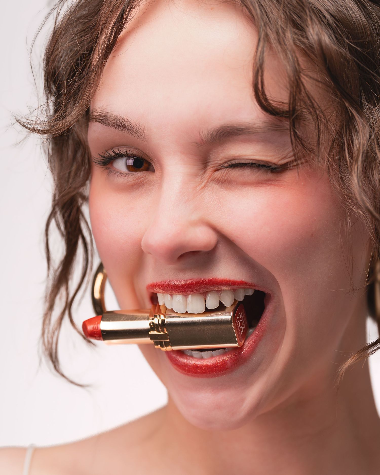 A sequence of close-up shots showing red lipstick being playfully held between teeth with a bright smile.
