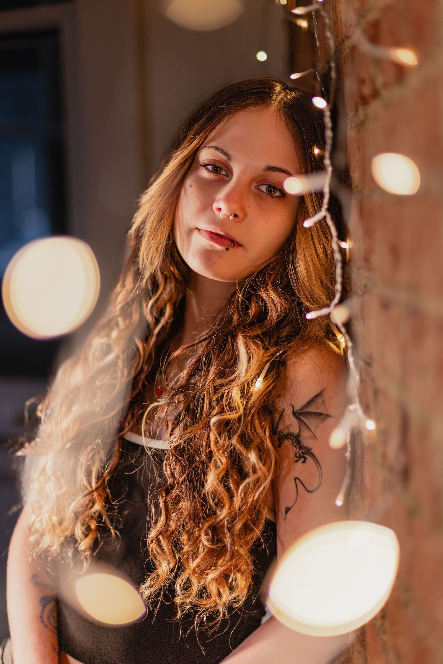 Artistic portrait with soft bokeh lights and warm tones showing curly hair illuminated by glowing string lights.