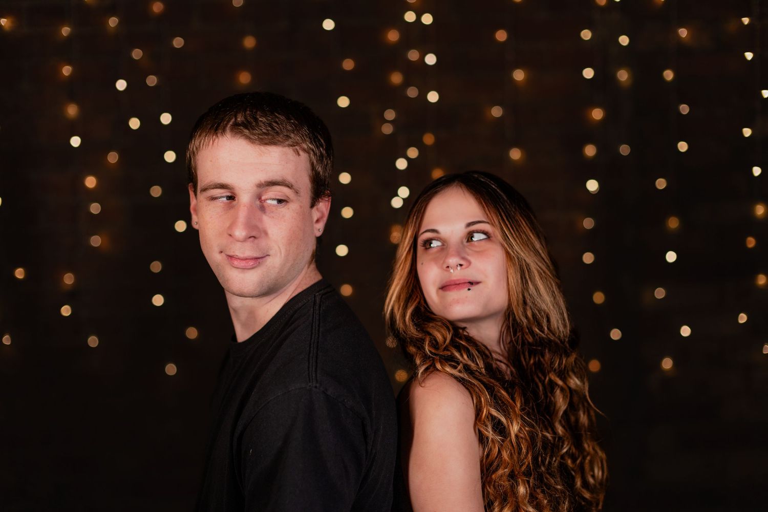 A couple poses together in front of glowing bokeh lights in a romantic evening setting.
