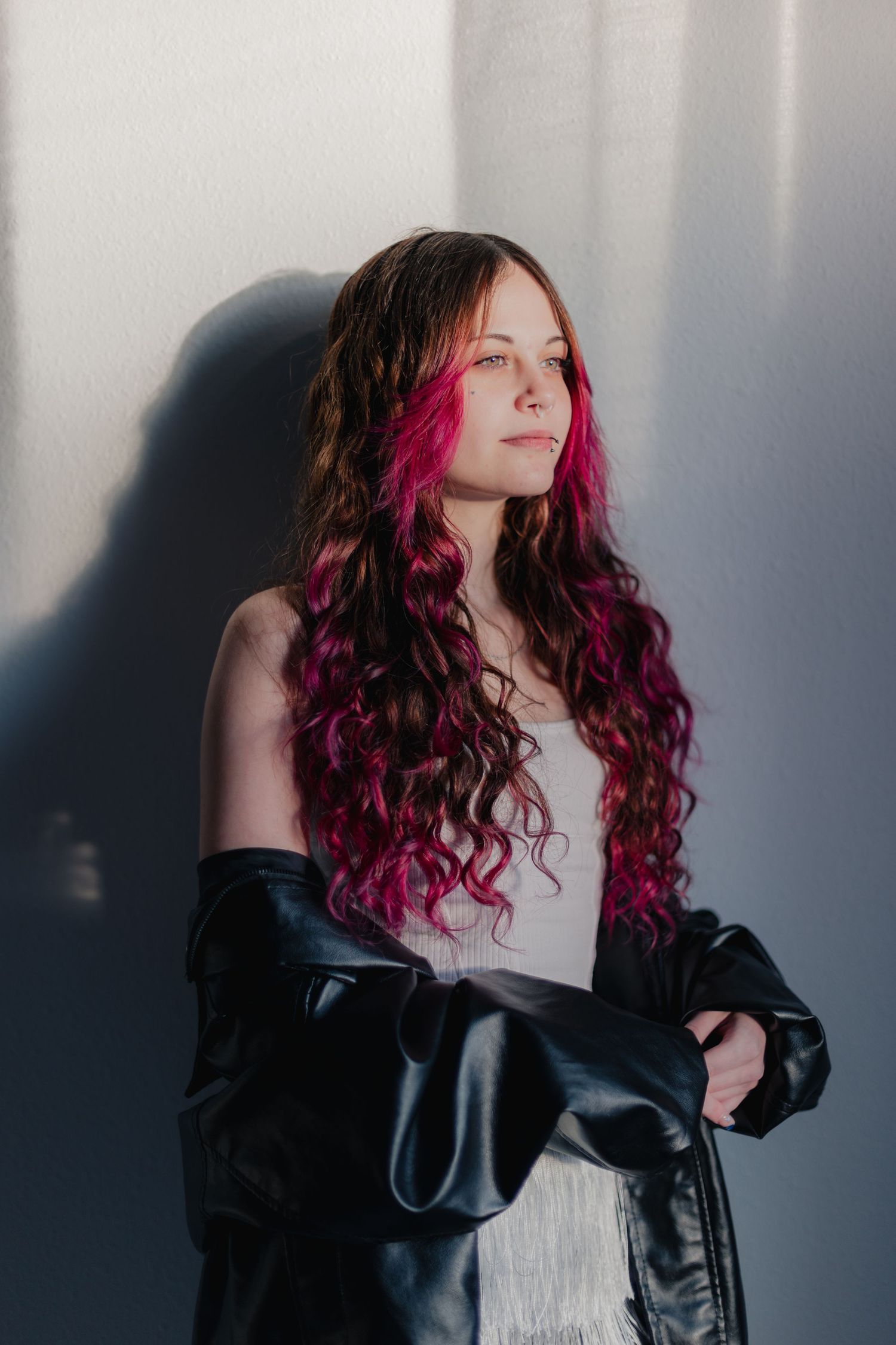 A series of moody portraits showing long curly hair with vibrant pink highlights against a dark background.