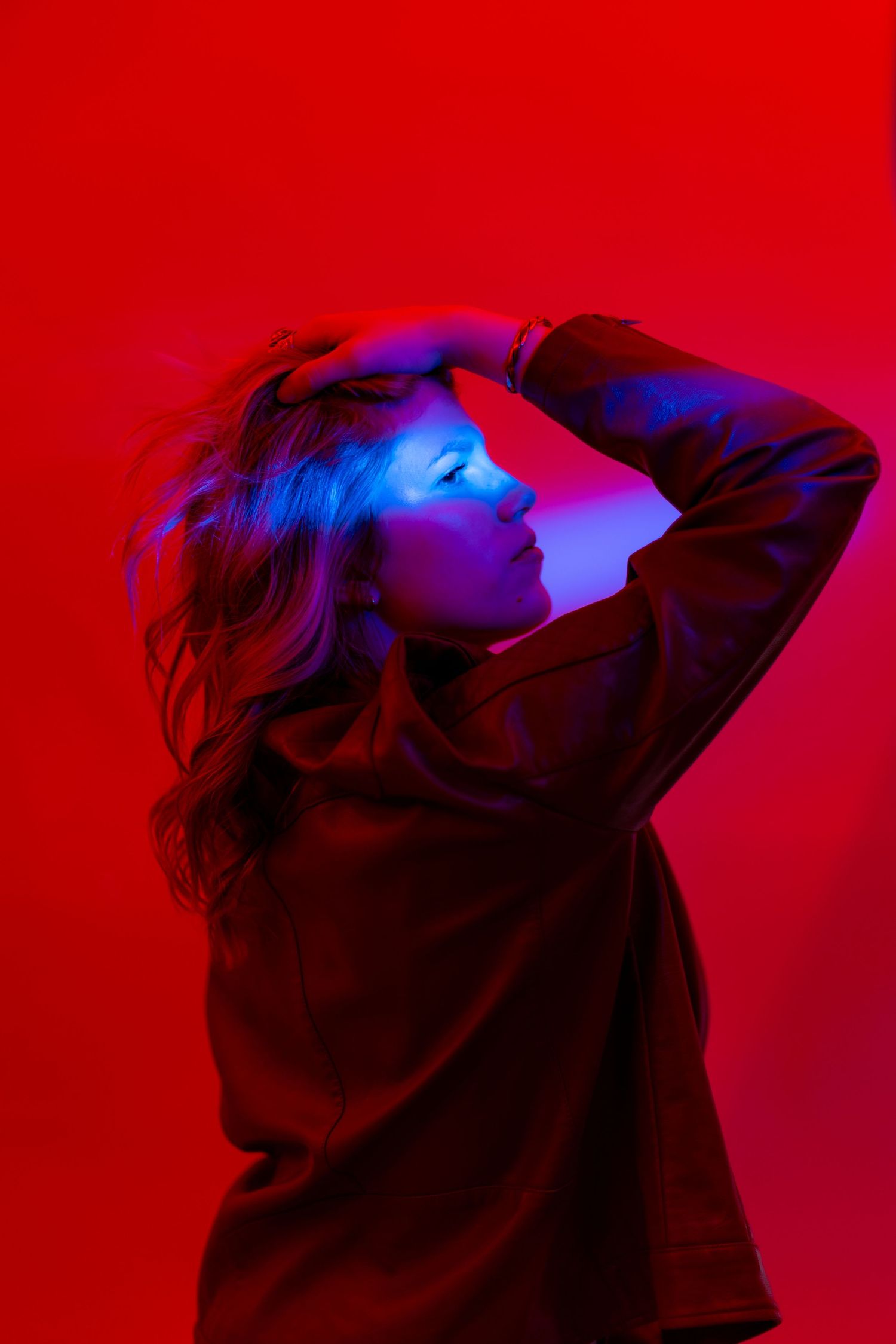 Artistic portrait series with silhouette against vibrant red background illuminated by blue light creating dramatic contrast.