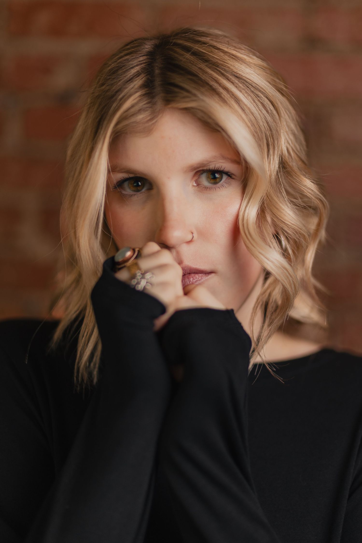 A series of moody portraits showing a person with blonde hair wearing a black sweater against a brick wall background.
