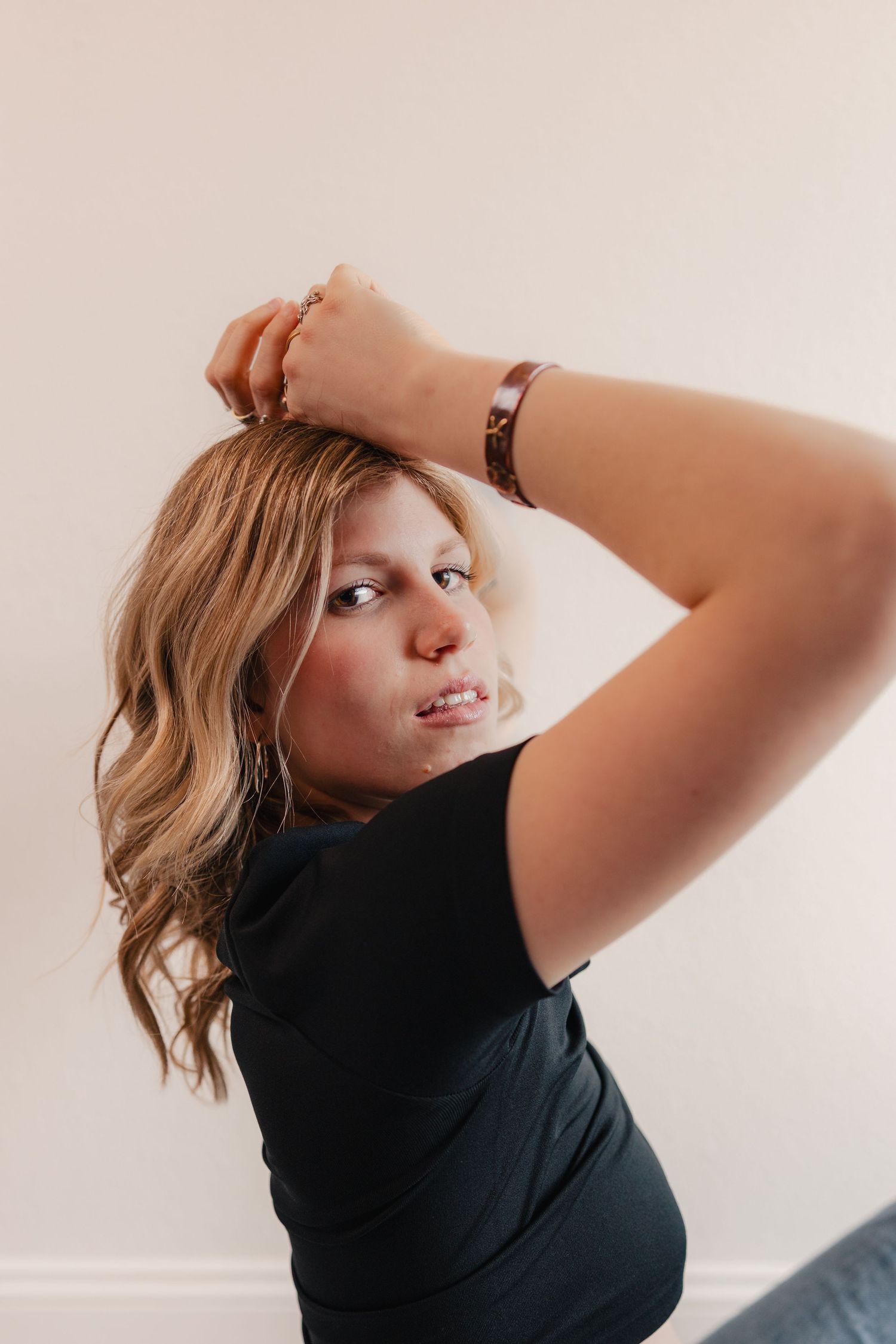 A person in a black shirt poses against a white background with dynamic movement and flowing blonde hair.
