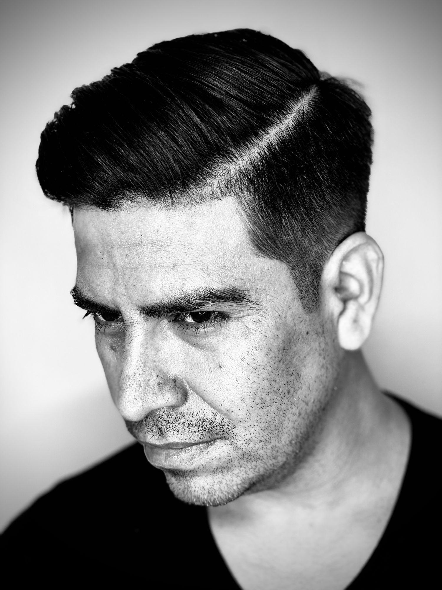 Black and white portrait photograph showing a side profile with short dark hair and a clean fade haircut against a light background.