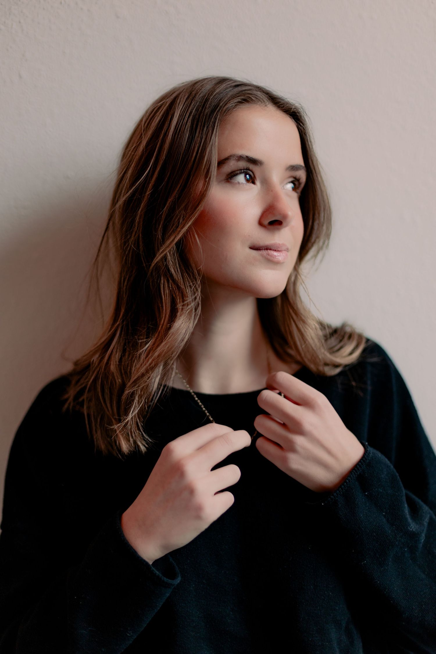 Artistic portrait looking up while wearing a black sweater against neutral wall.