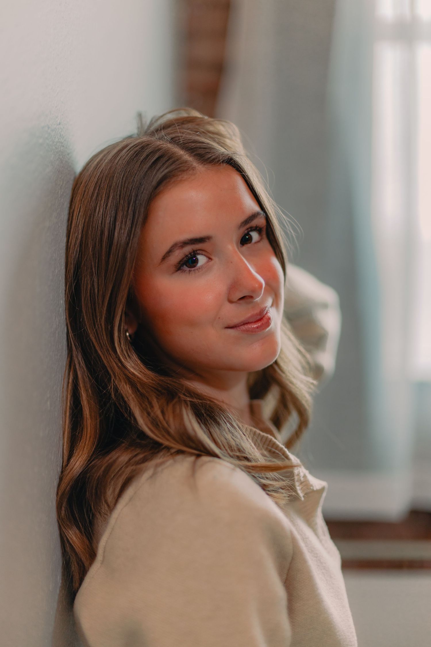 Casual lifestyle portrait against a wall wearing a neutral colored sweater with soft natural lighting.