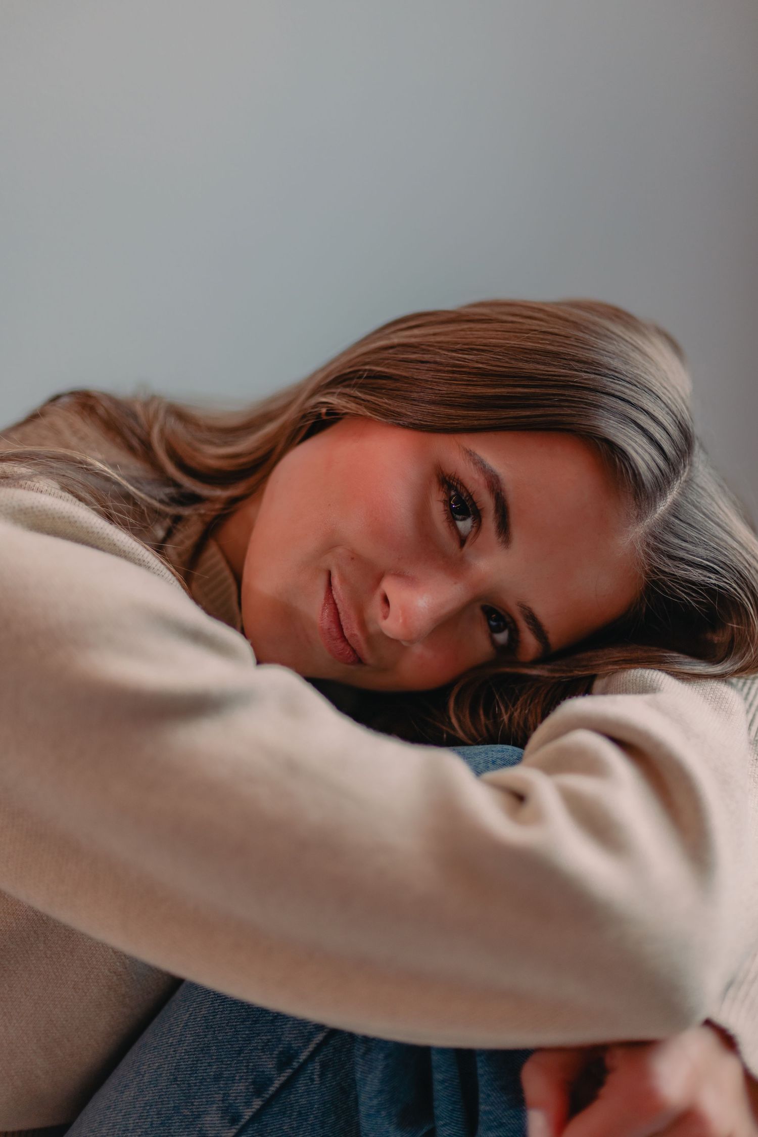 Portrait of someone in a beige sweater resting their head while smiling warmly at the camera.