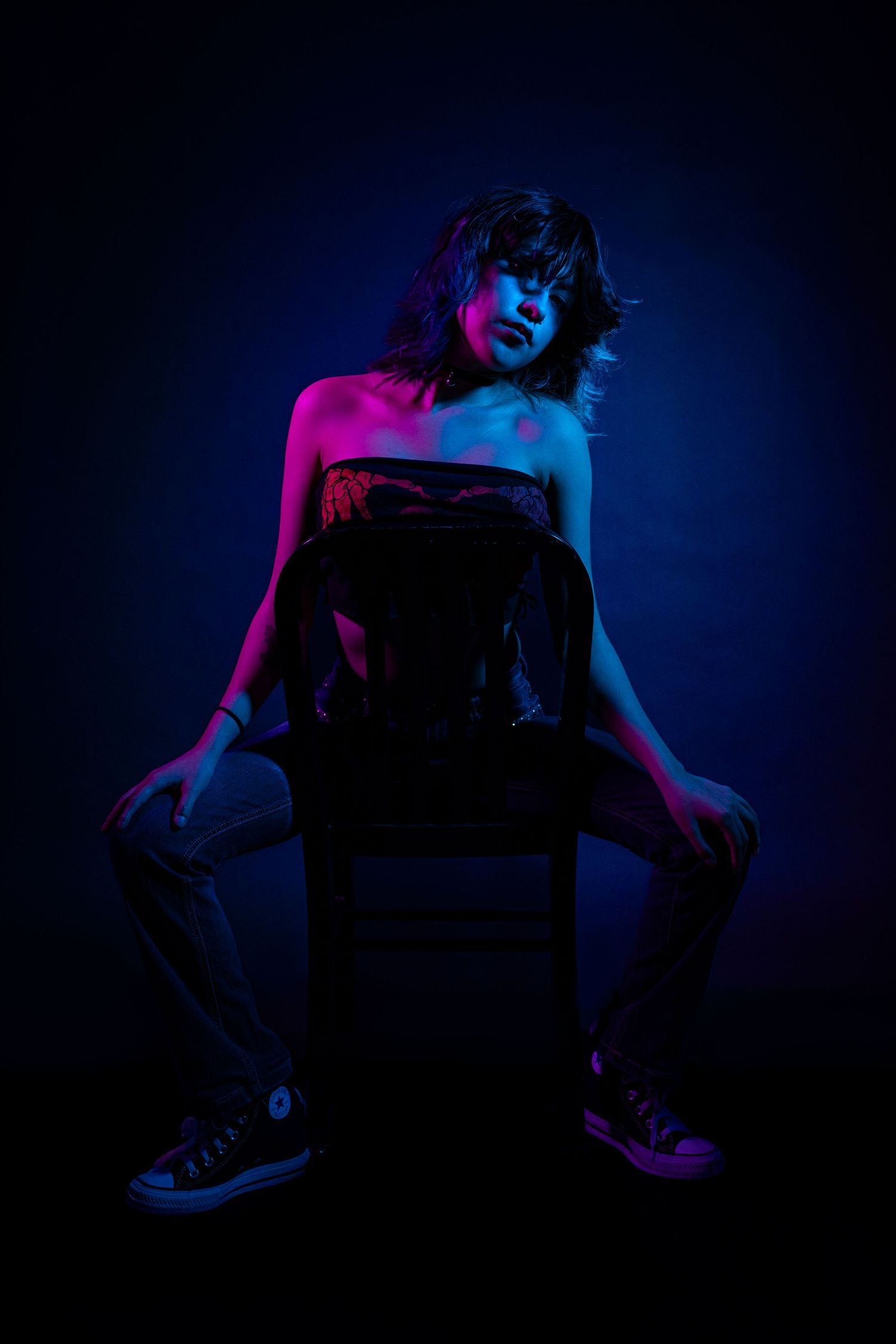 Silhouetted figure in dramatic lighting poses on chair against dark background with blue and pink neon accents.