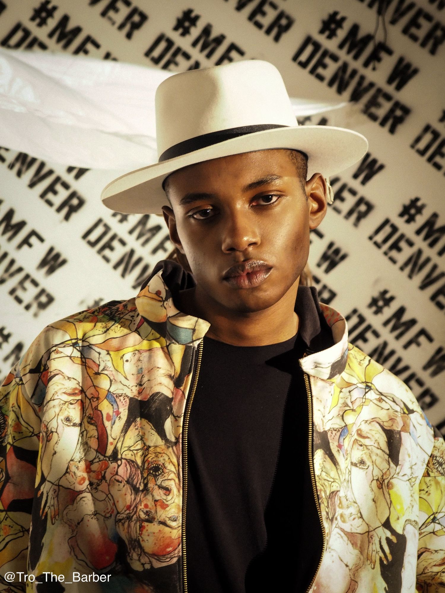 A person wearing a black shirt and white hat poses against a wall with repeating text pattern in a stylized photo series.