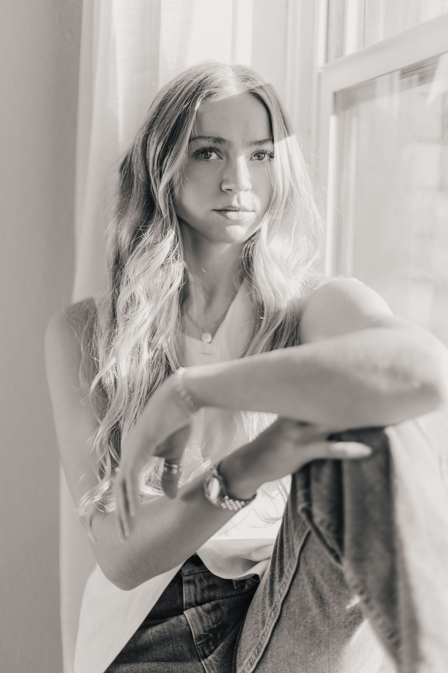 A series of black and white fashion portraits showing a woman with blonde hair posing in a dark top by a window.