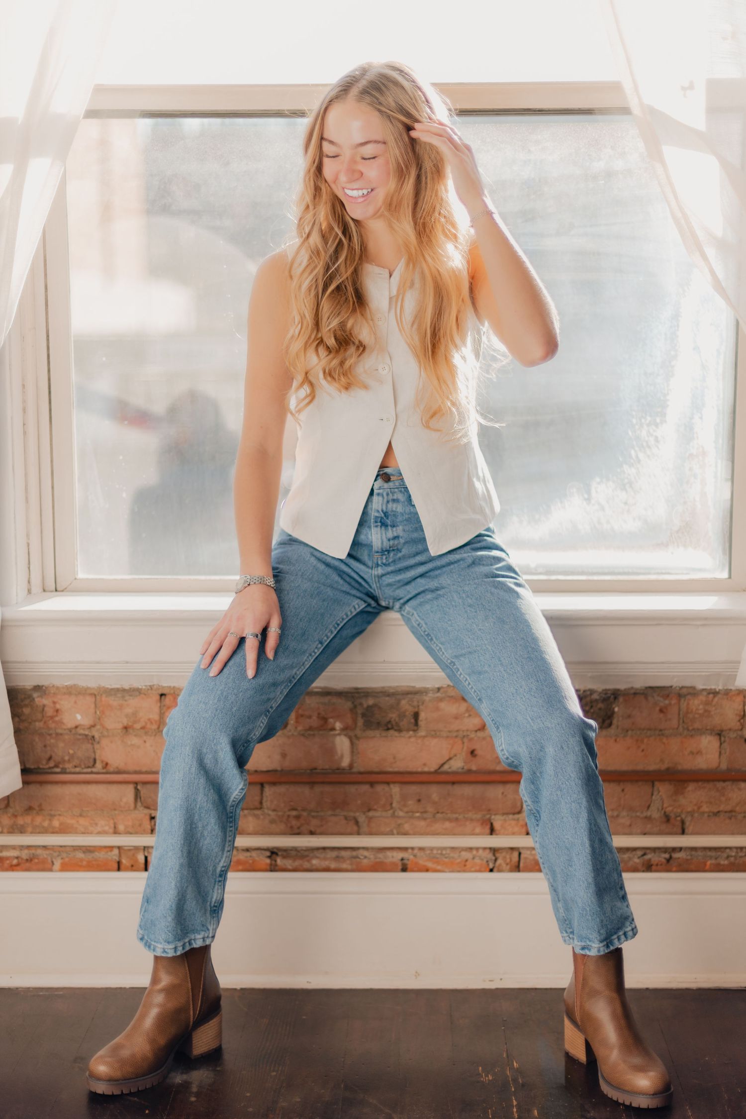 Person in light vest and jeans sits casually by window with brown boots in series of relaxed poses.