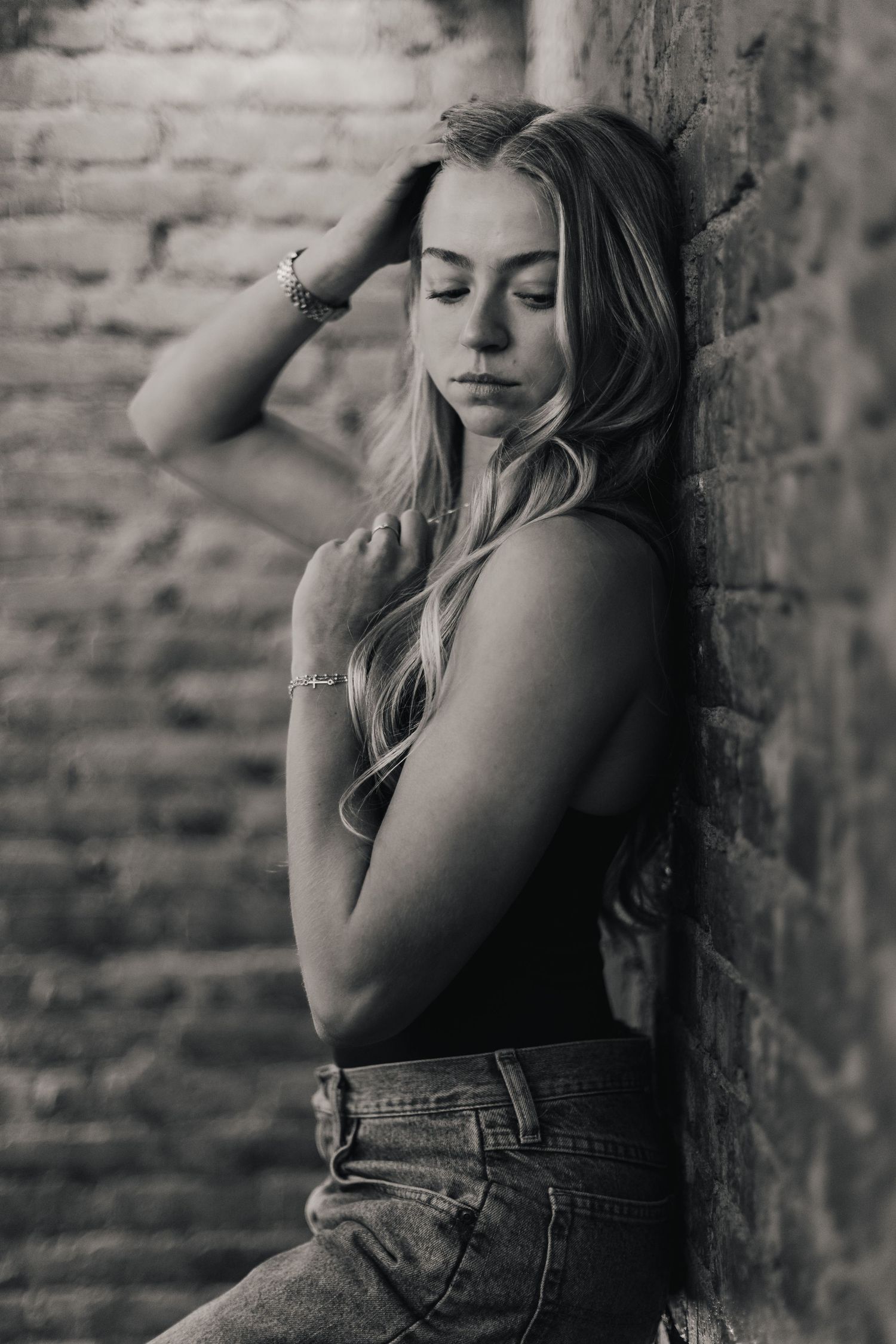 Black and white artistic portrait series showing woman in denim against brick wall in contemplative poses.