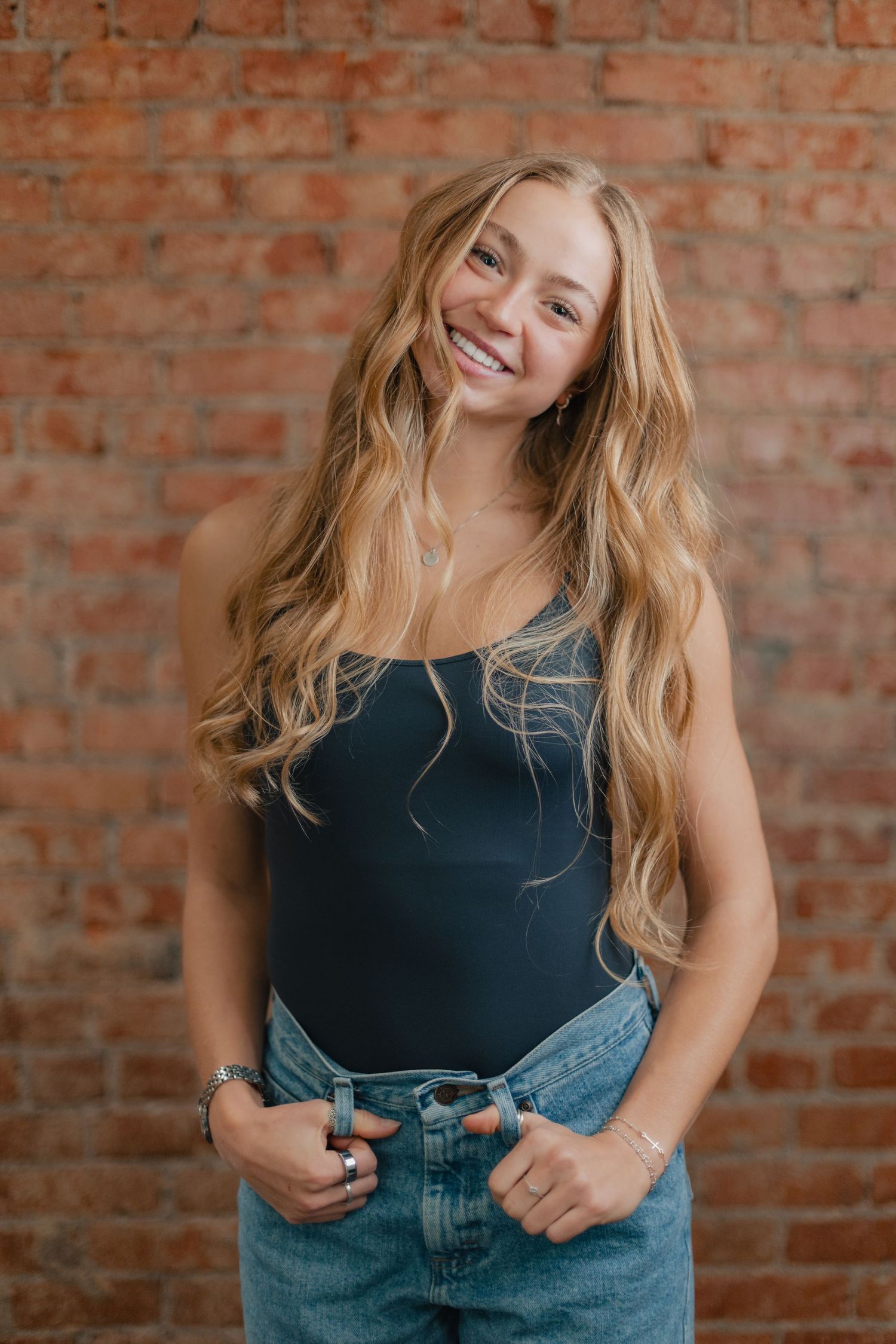 A sequence of lifestyle portraits showing someone in a navy top and denim against a rustic brick wall background.