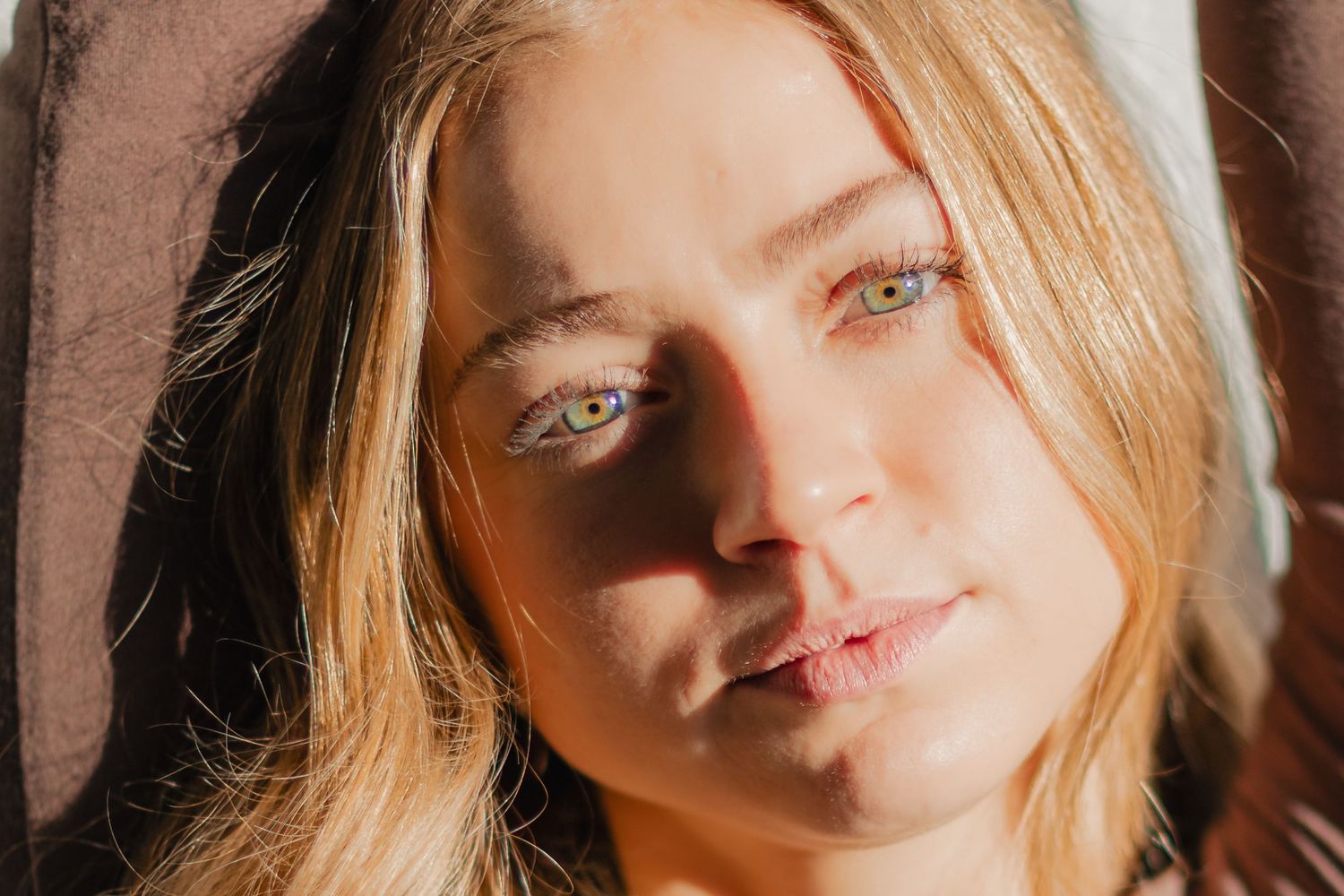 A close-up portrait of a person with blonde hair and blue eyes in warm sunlight.