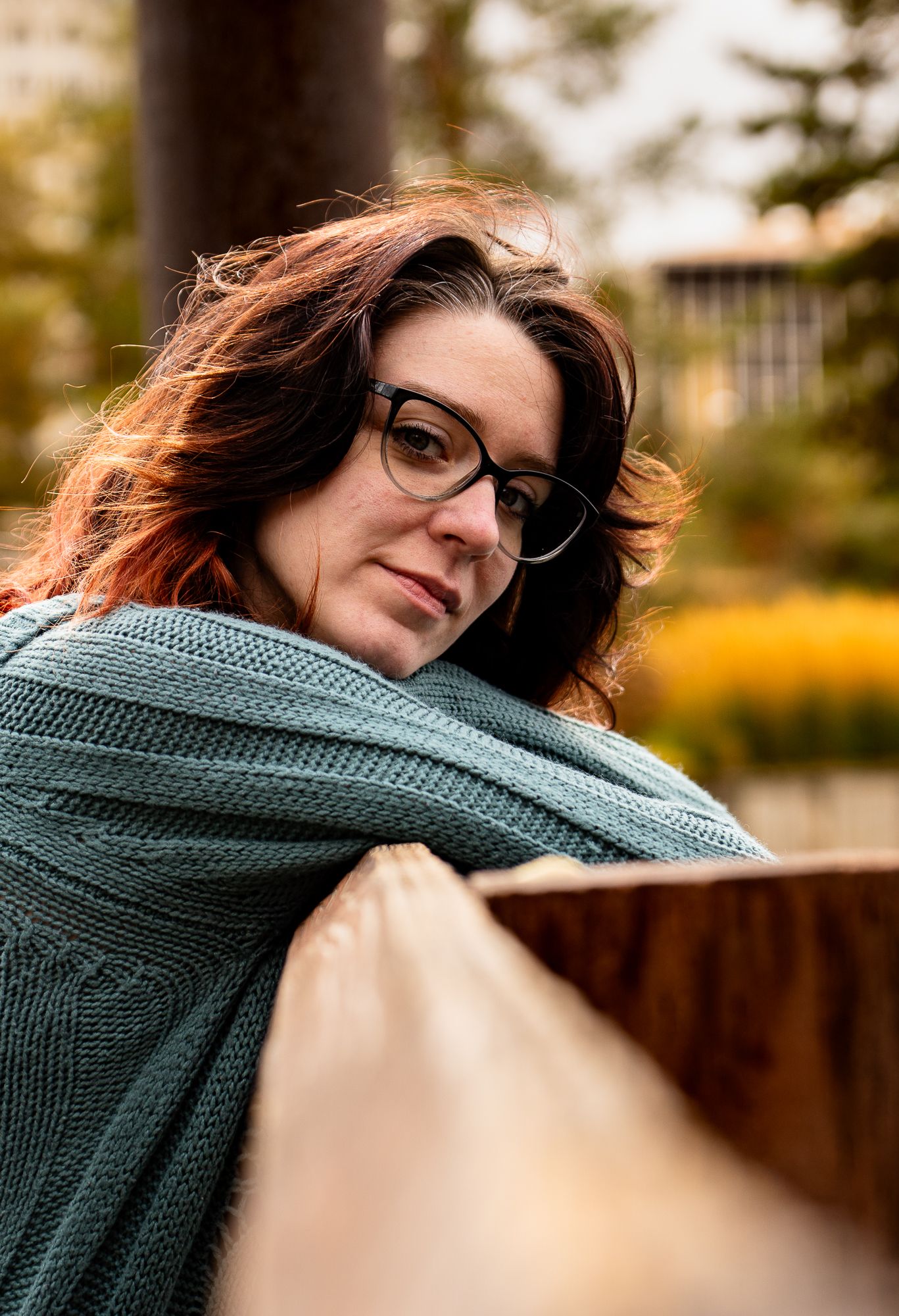 A person wearing glasses and a teal knit sweater poses in a series of outdoor portrait shots with warm autumn lighting.