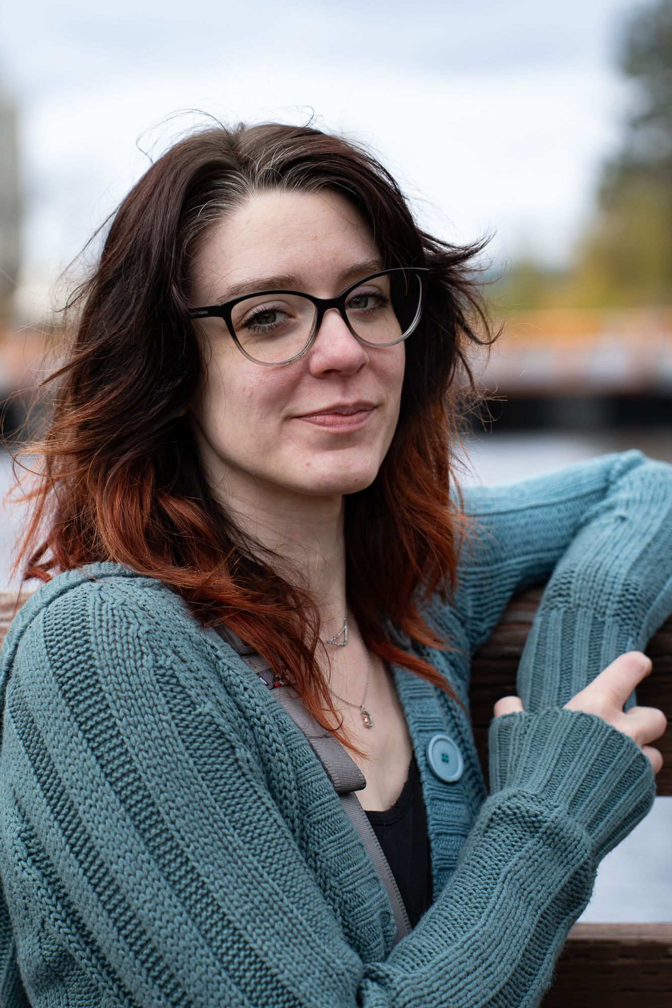 A person in glasses and a teal sweater poses outdoors in a series of casual portraits.
