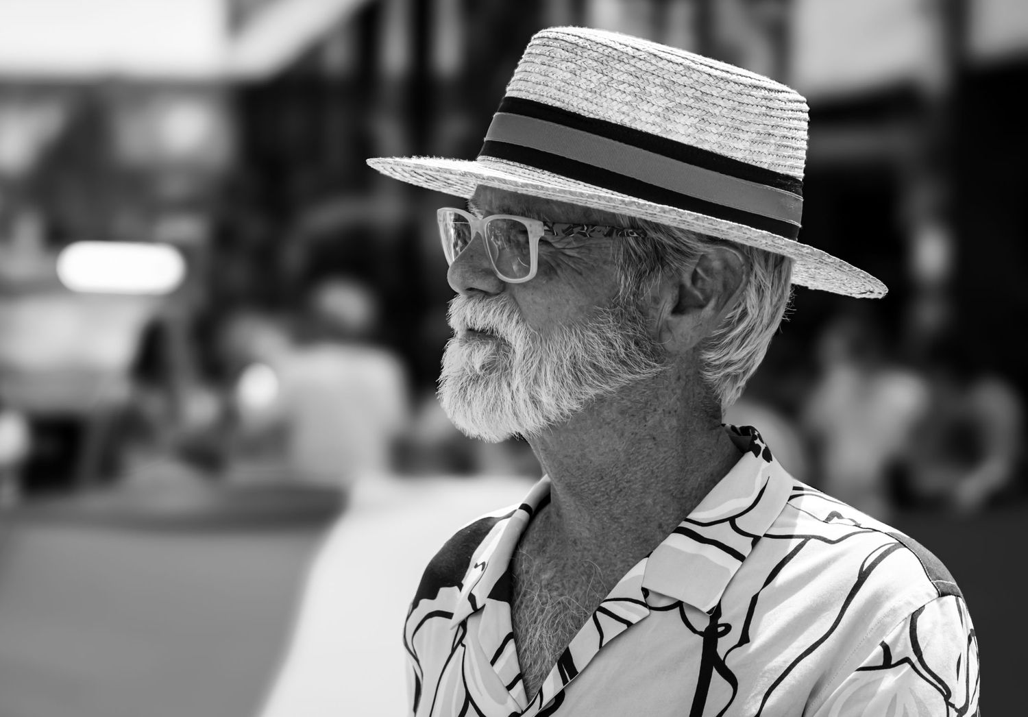 Black and white portrait of a person wearing a straw hat and glasses with a white beard in a patterned shirt.