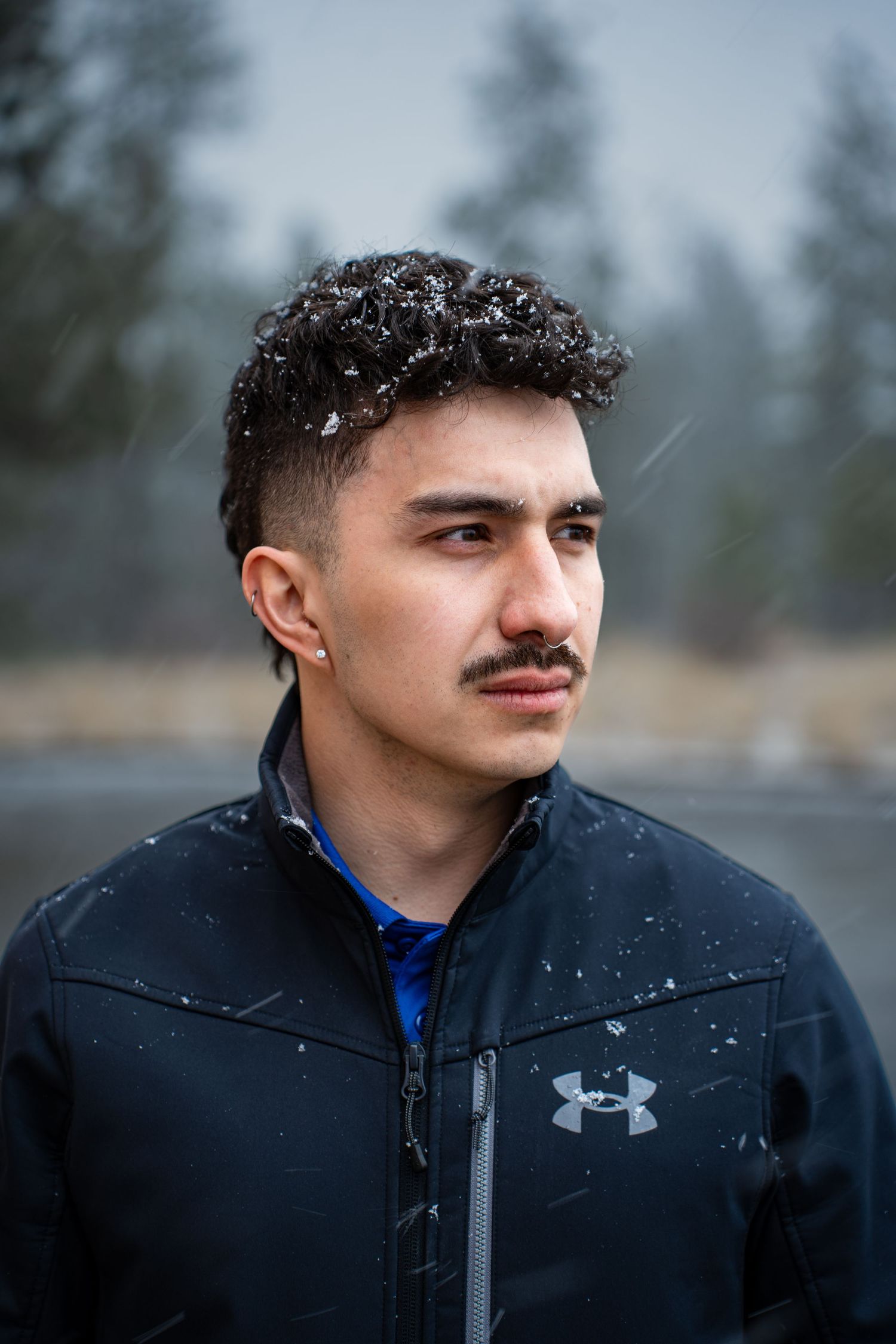 A person wearing an Under Armour jacket poses in a snowy outdoor setting with trees in the background.