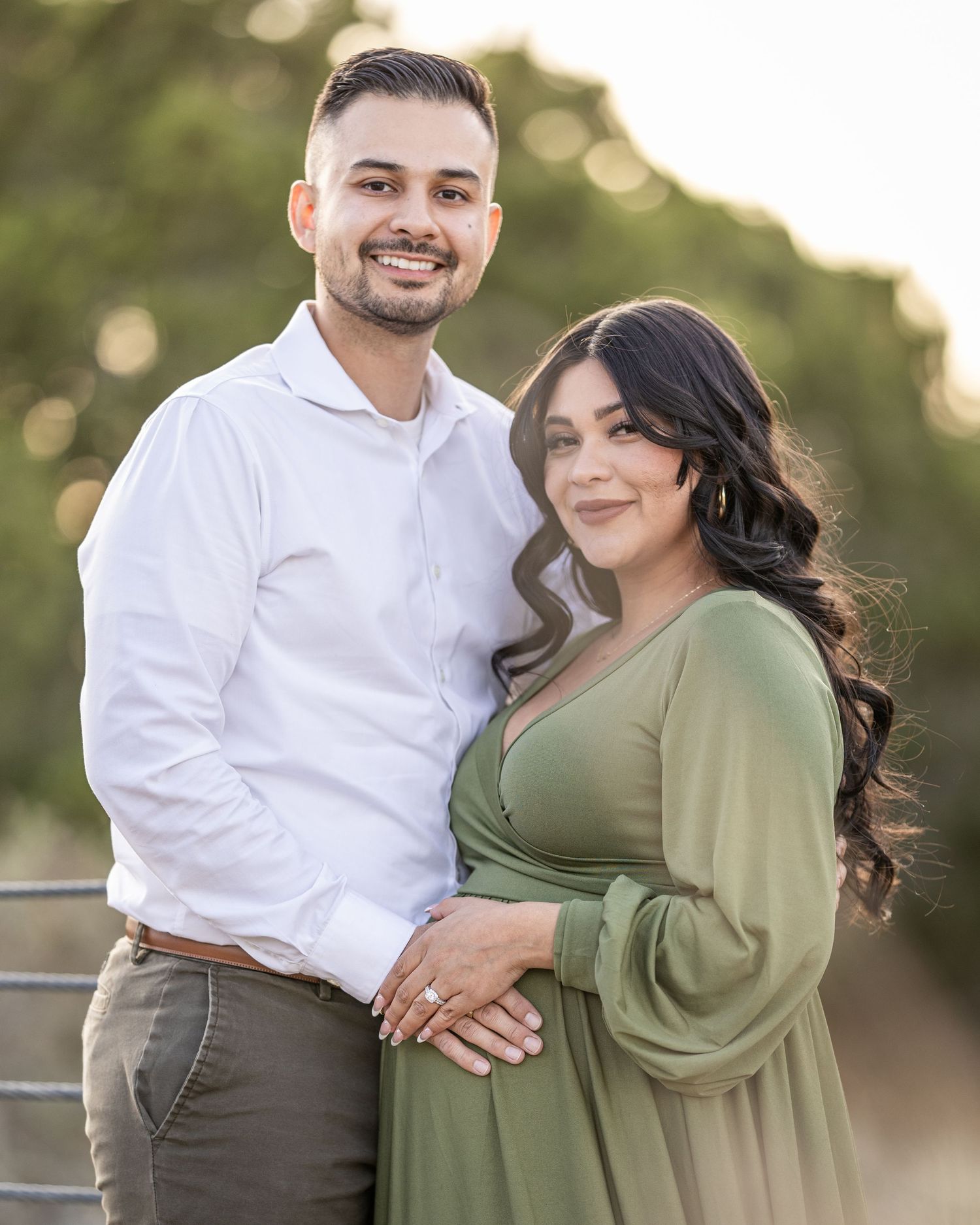 A couple poses closely together during a maternity photoshoot. The portrait of the couple captures the couple during golden hour.