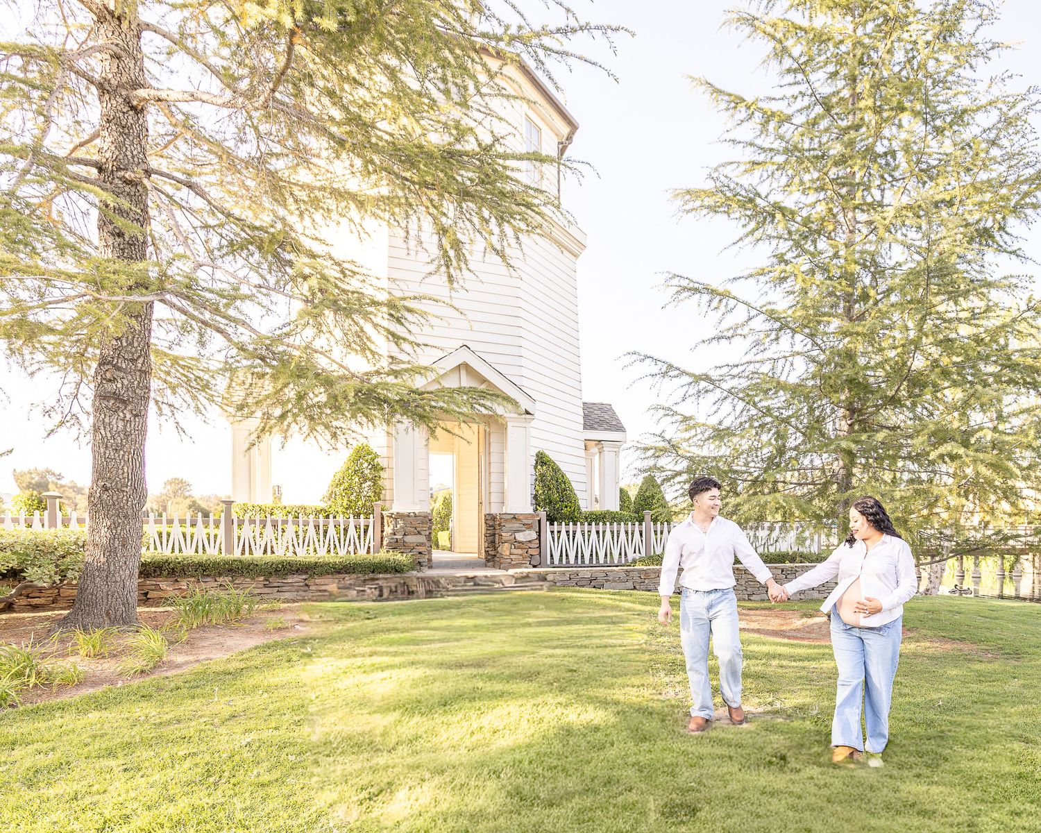 A couple poses and walks for a maternity photoshoot. A professional photographer uses natural light outdoors to photograph couple.