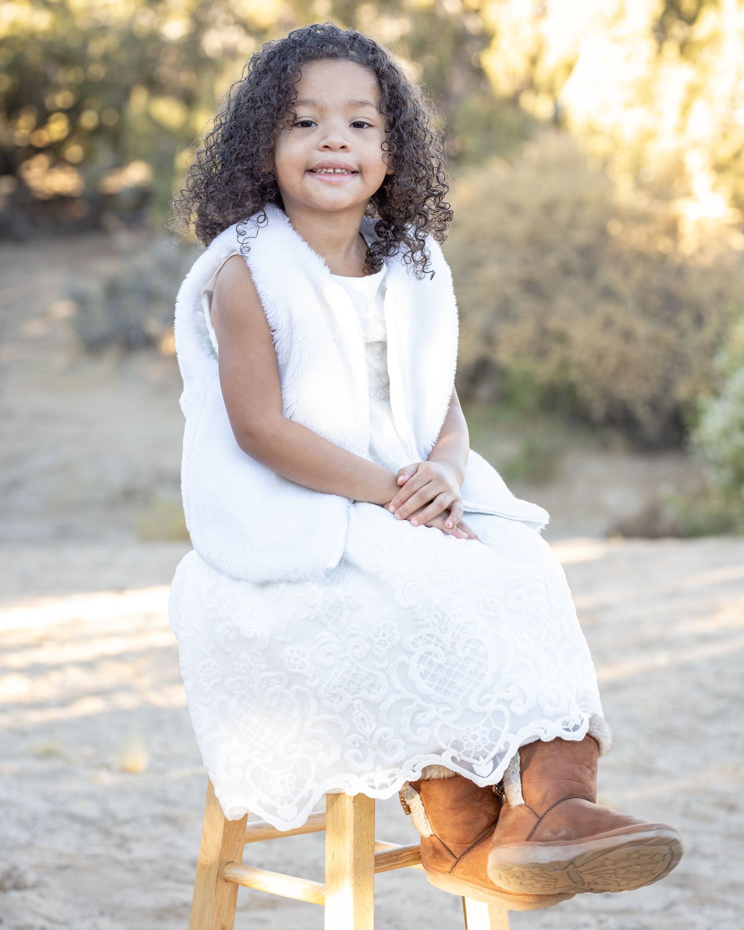 A young child poses for a portrait while sitting on a wooden stool during golden hour.