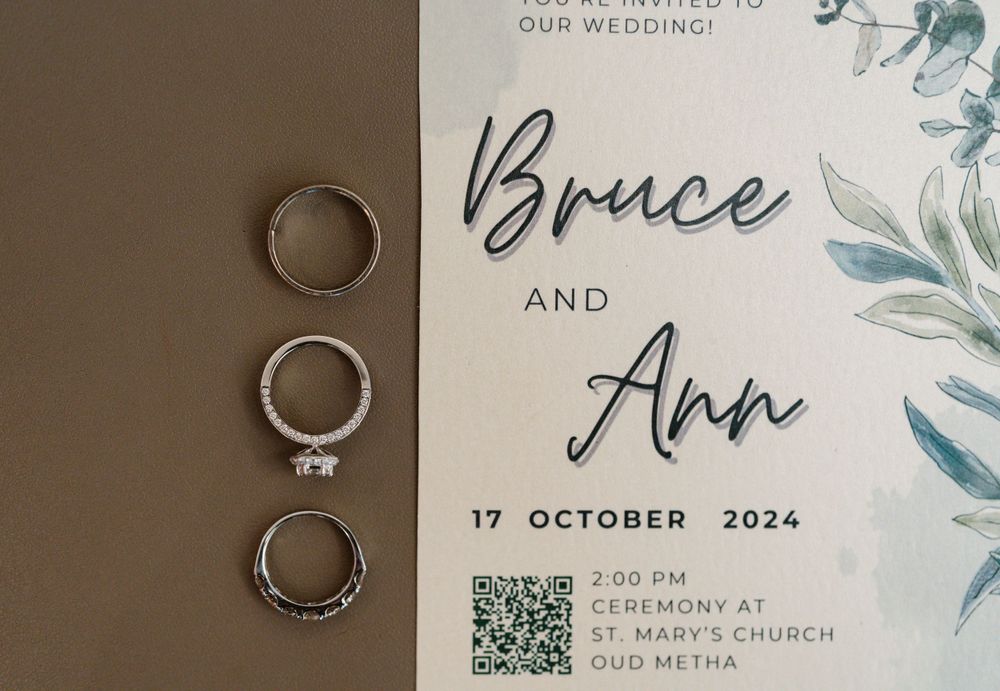 Wedding invitation for Bruce and Ann with wedding rings photographed on brown background.