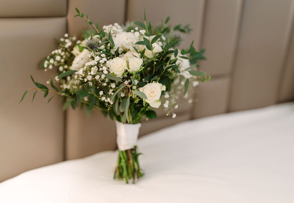 Elegant white rose and baby's breath wedding bouquet with green foliage on beige leather.