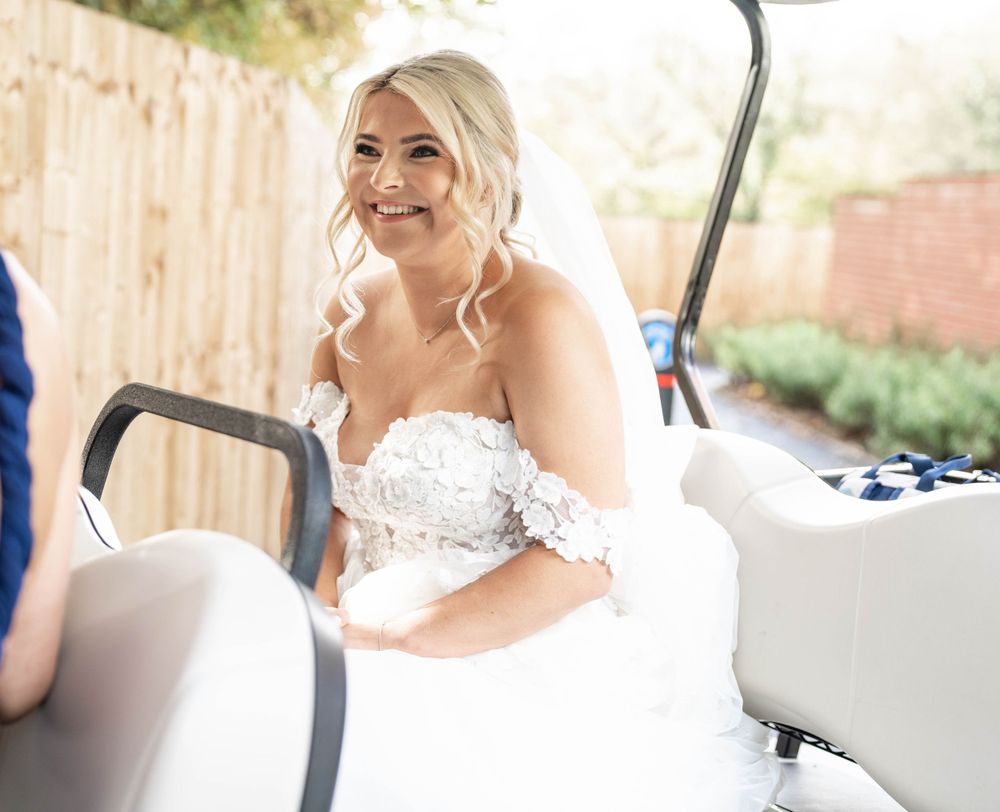Bride in white strapless wedding dress smiles while seated in a golf cart.