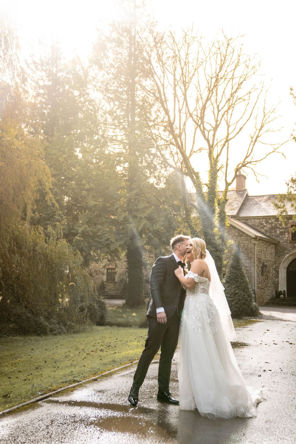 Dreamy backlit wedding portrait on rainy path with golden sunset glow.