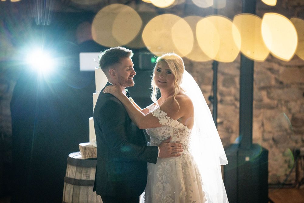 First dance under warm lighting with rustic stone wall backdrop.