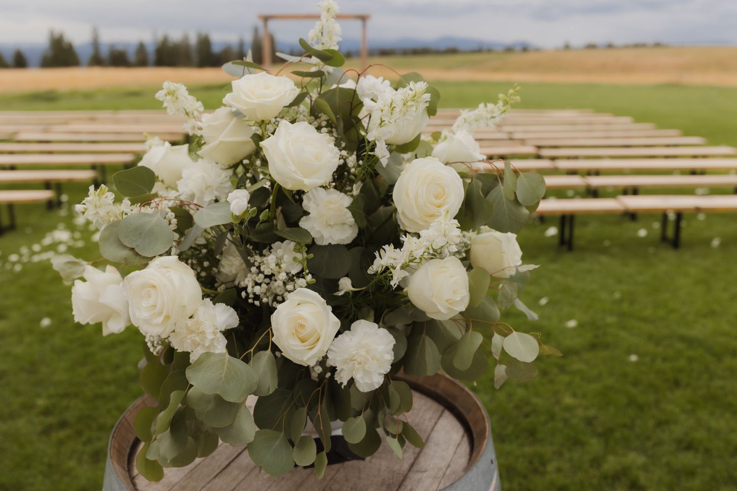 White rose and greenery wedding centerpiece arrangement on outdoor wooden benches. Spokane wedding photographer.