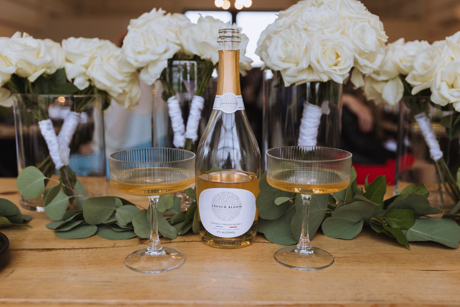 Champagne bottle and glasses arranged with white roses and eucalyptus leaves. Spokane wedding photographer.