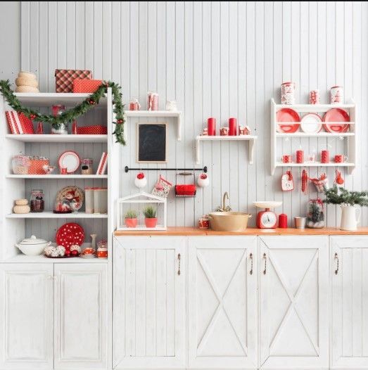 White kitchen with red holiday decor, shelves displaying festive ornaments and Christmas decorations.