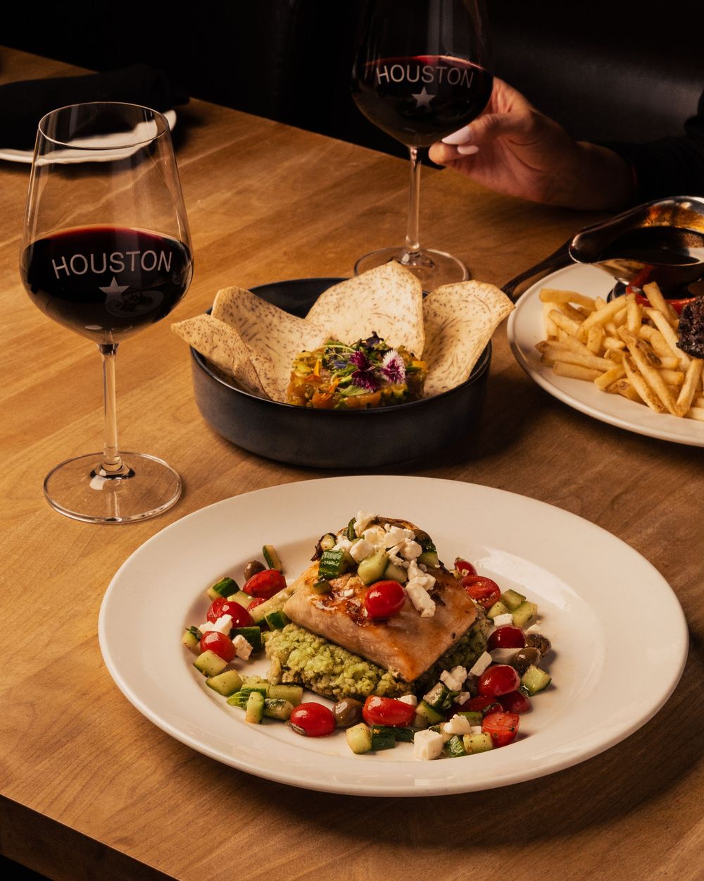 Fine dining table with wine glasses, a salmon salad, french fries and wrapped sandwiches in a restaurant setting.