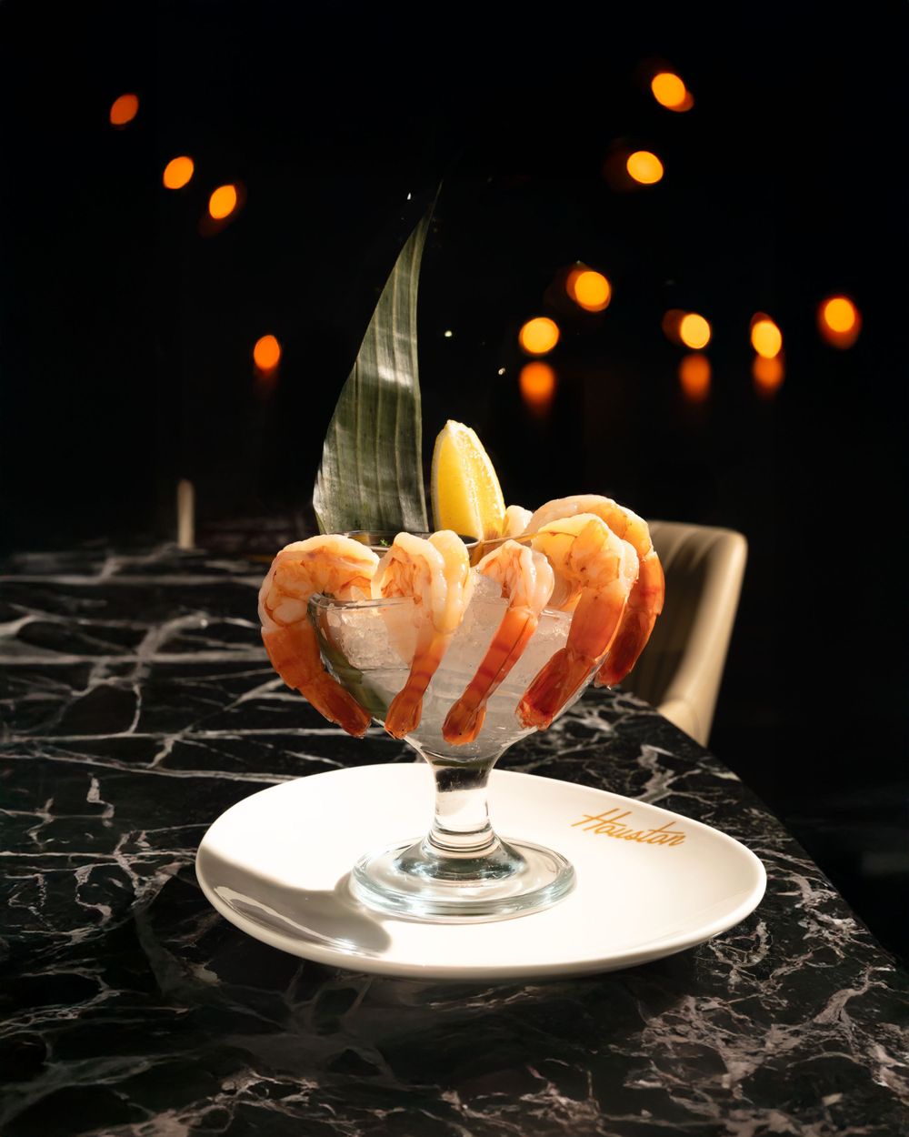 Fresh shrimp cocktail arranged in a glass with citrus and decorative leaf on black marble surface. Mtlshutter photography
