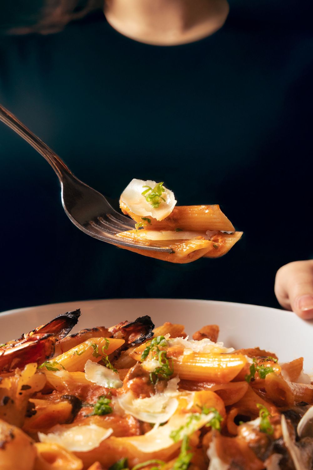 Close-up of fork lifting garnished pasta from a dish with creamy sauce. Mtlshutter photography