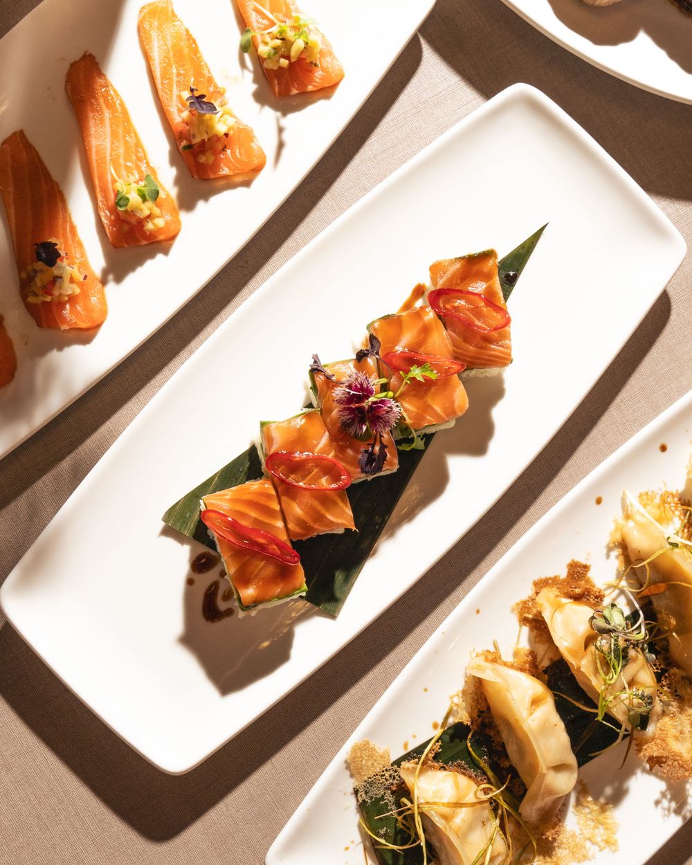 Row of fresh salmon appetizers garnished with microgreens on long white serving plates. Mtlshutter photography