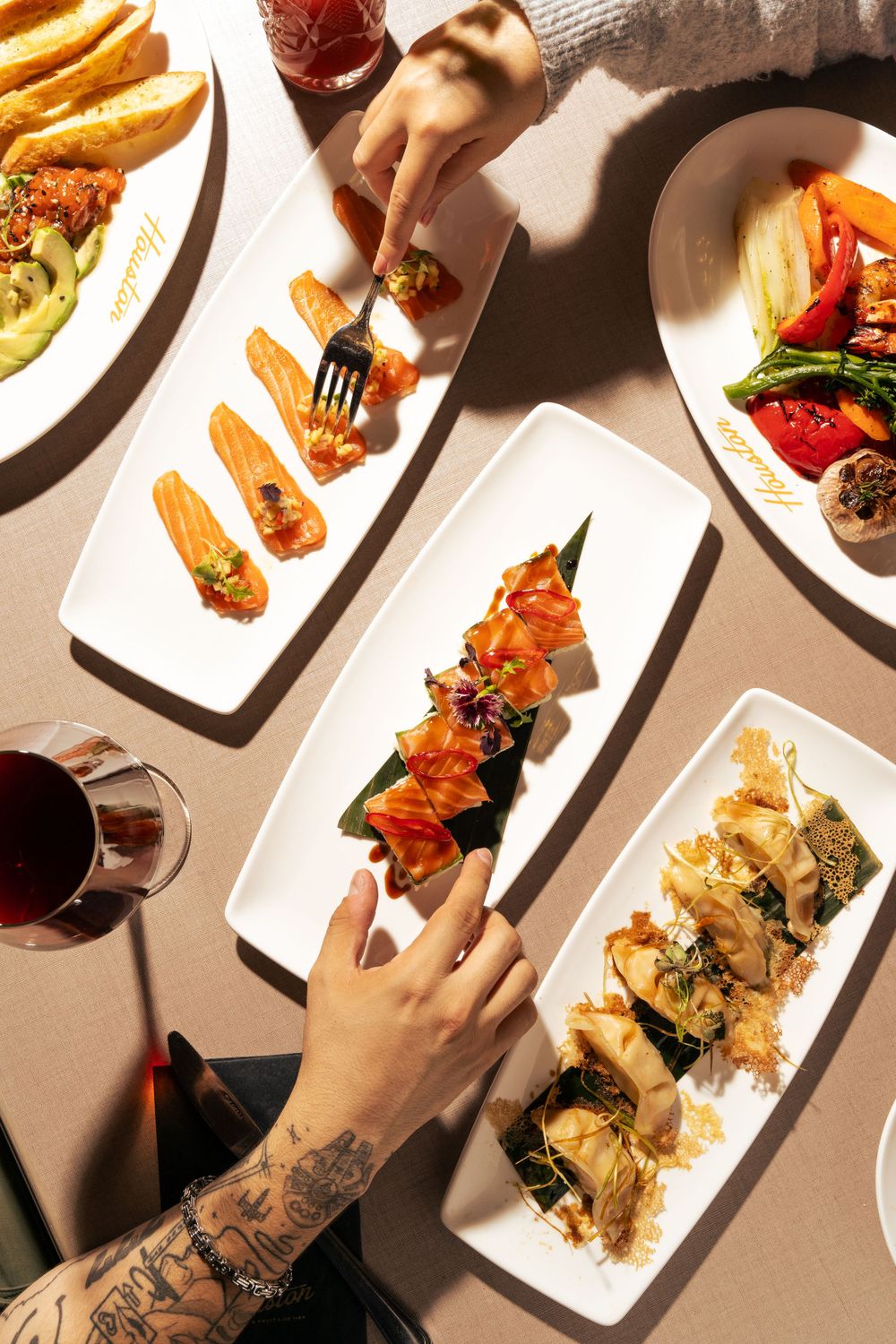Overhead view of multiple appetizer plates with wine glasses on a sunlit dining table. Mtlshutter photography