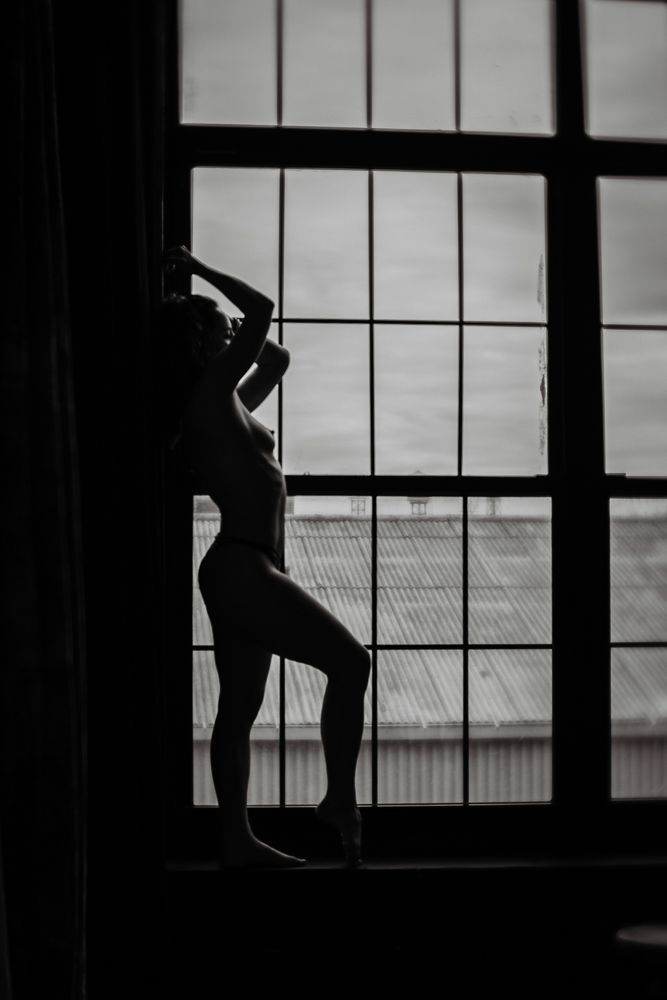 Dramatic silhouette of a figure posing in window frame with geometric shadows.