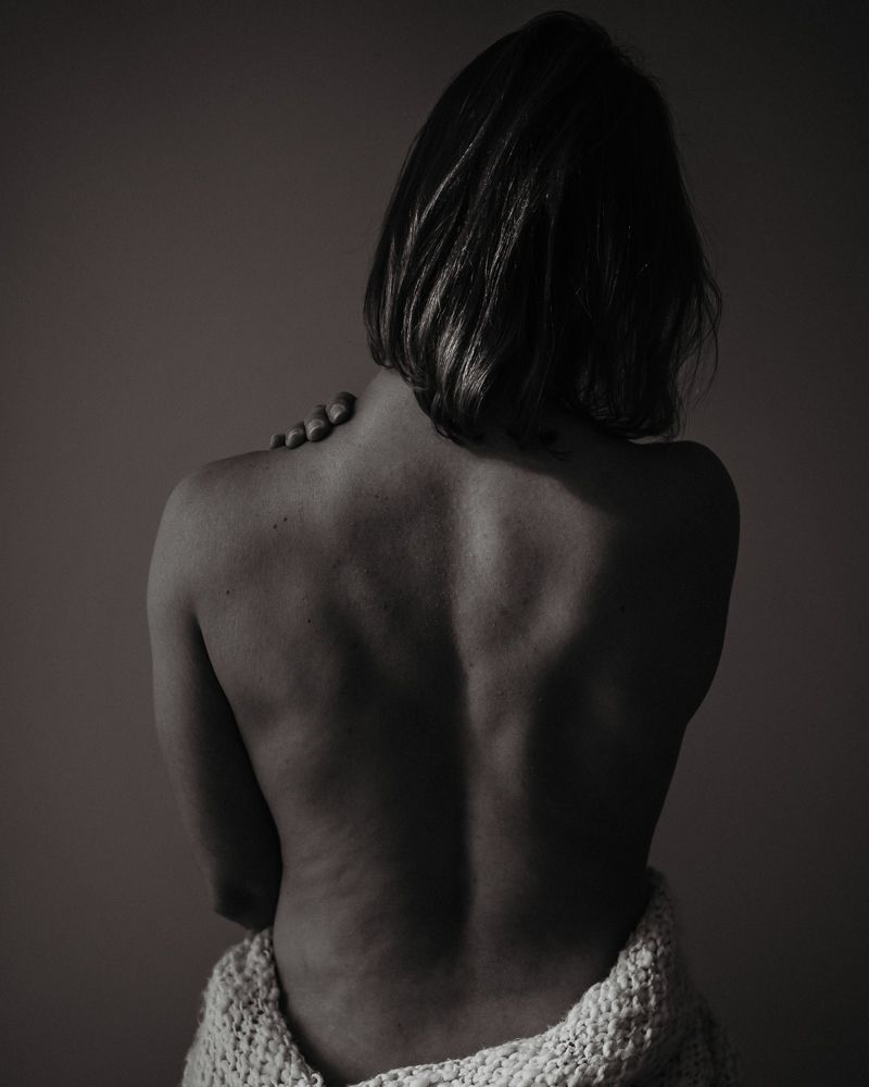 Artistic black and white photograph of a bare back with knit fabric below.