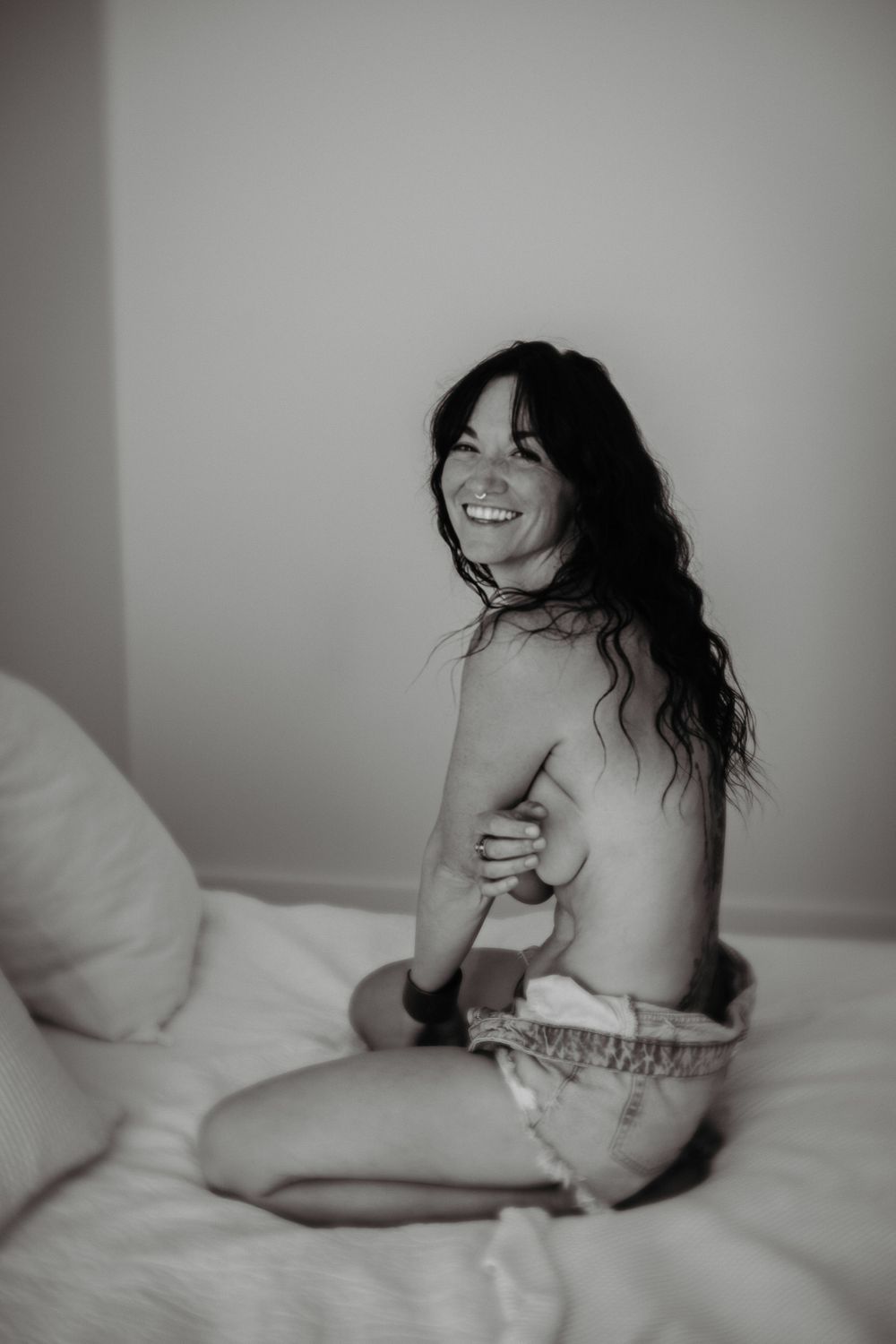 Candid boudoir portrait showing joyful genuine emotion on white bedding.