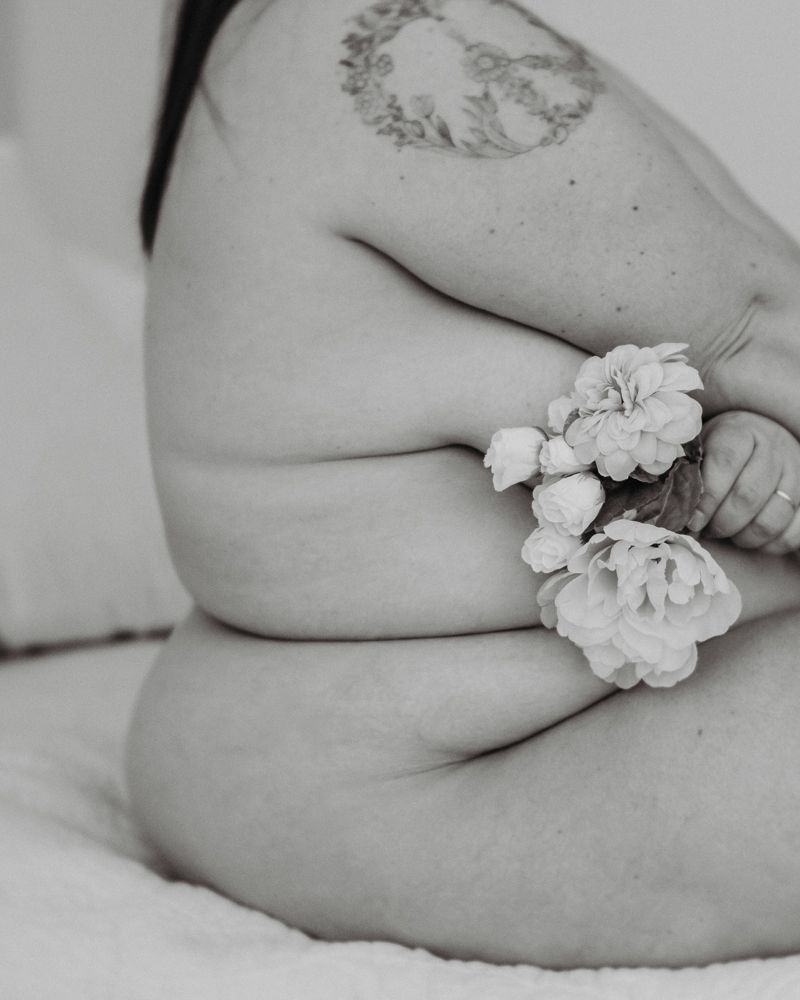 Artistic nude study with white flowers against skin in black and white.