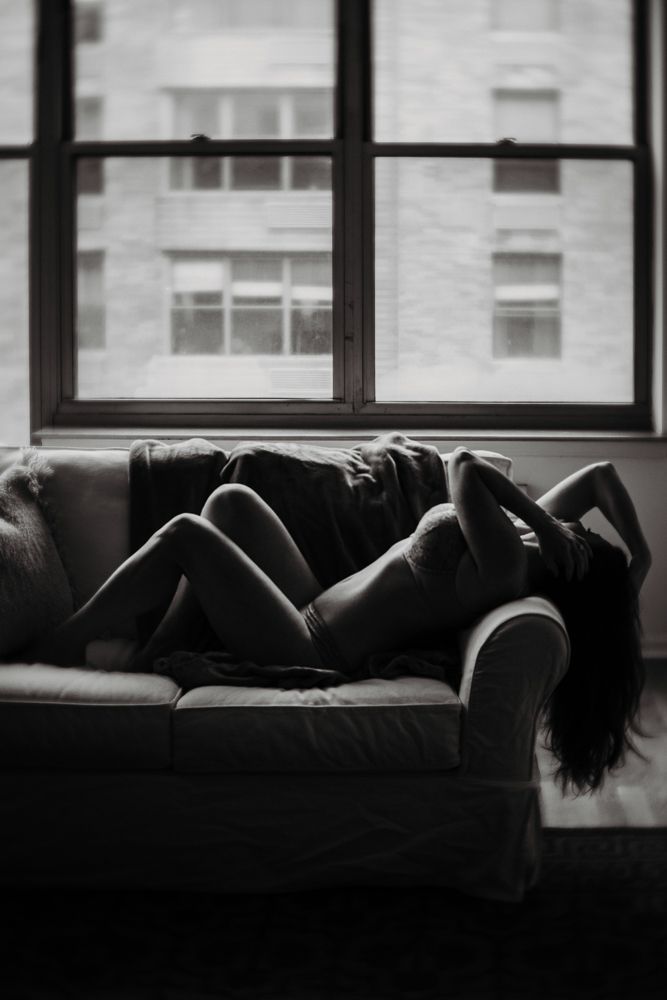 Silhouette of person reclining on couch near window in moody black and white lighting.
