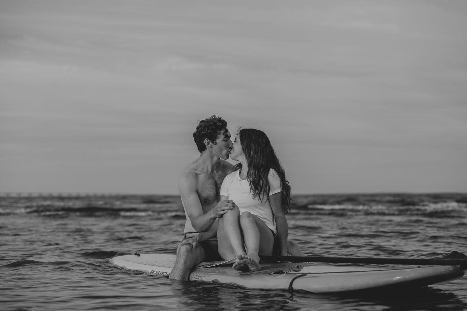 Couple sit on a paddleboard in the ocean and share a kiss in Chelton, PEI, Canada.