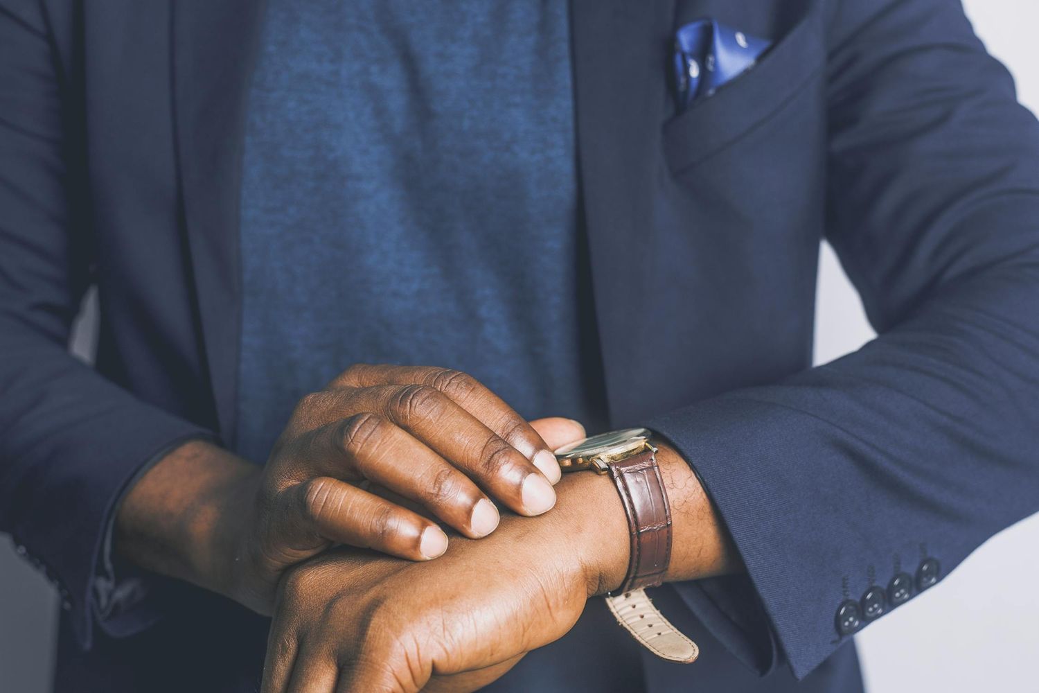 Close-up of hands checking time on wristwatch while wearing dark business attire.