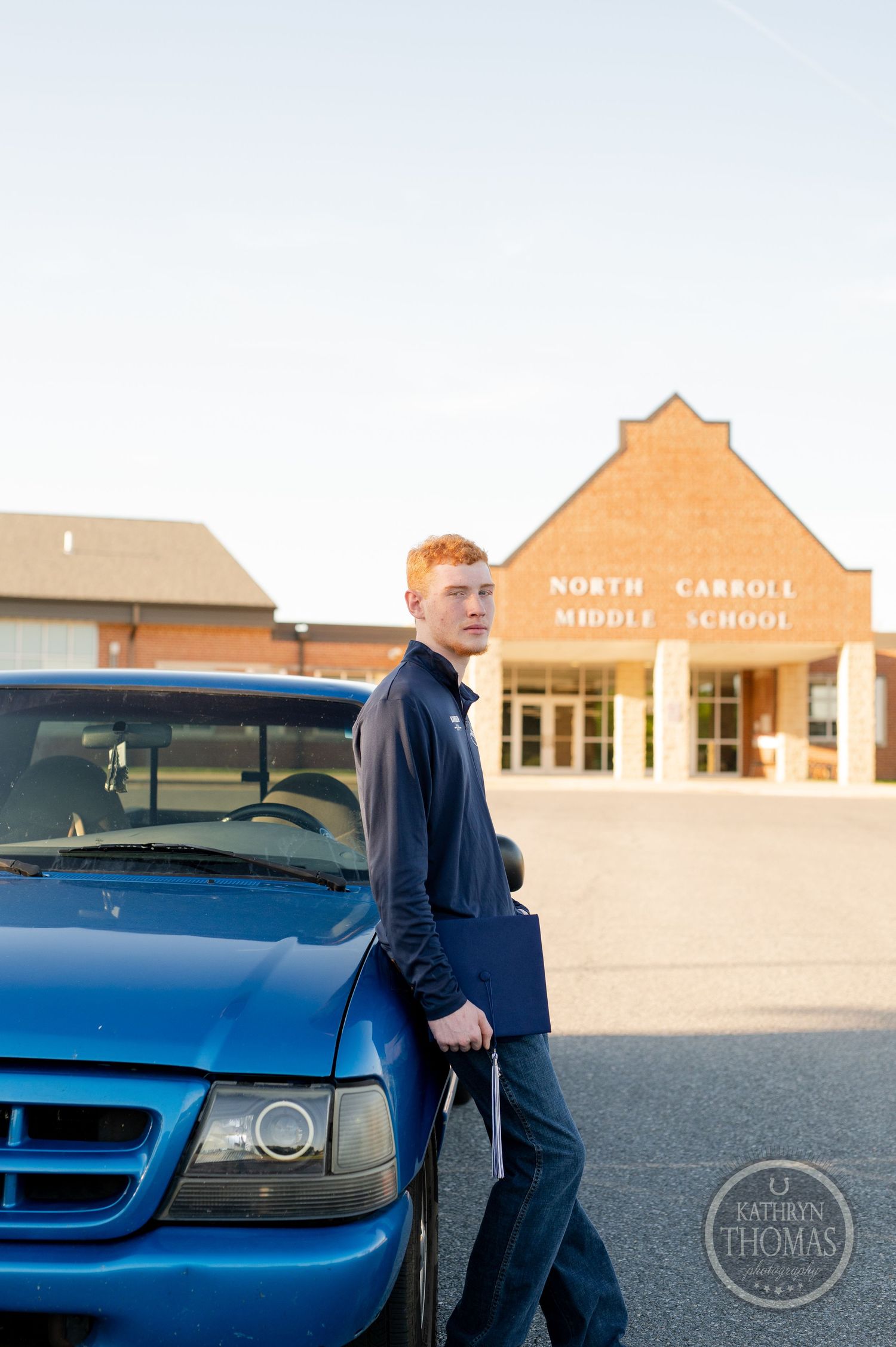 Graduate in navy jacket poses beside blue truck at North Carroll Middle School.