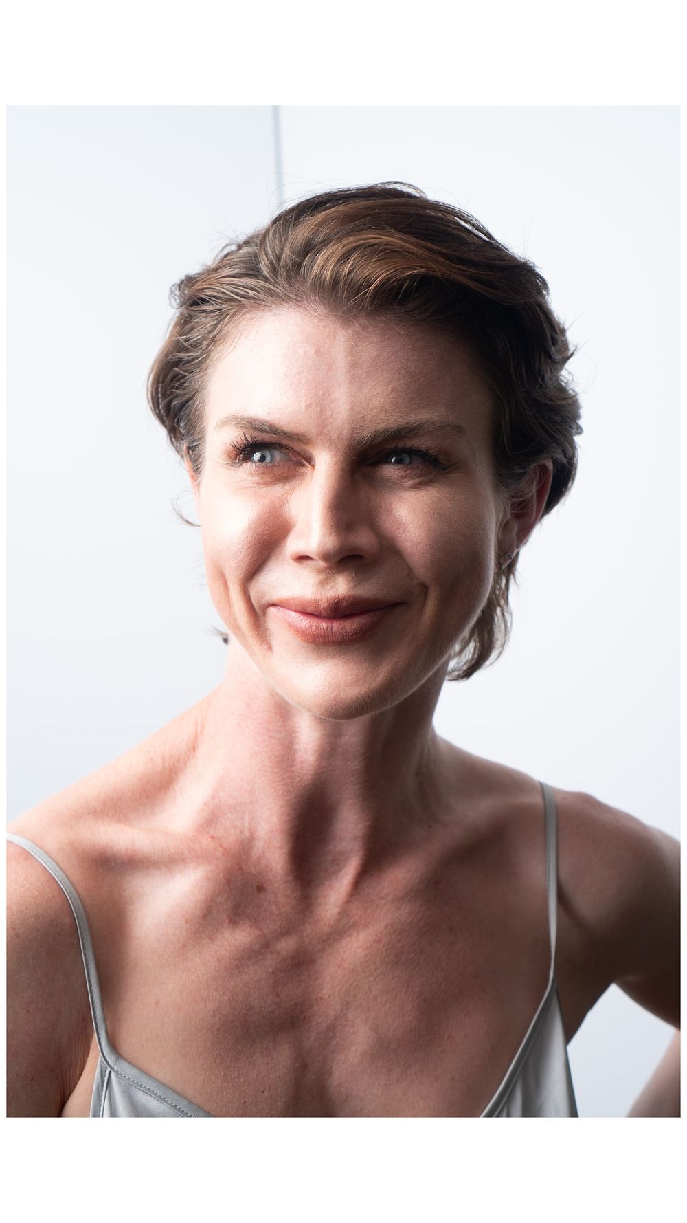 Portrait of person in gray tank top with short styled hair against white background.