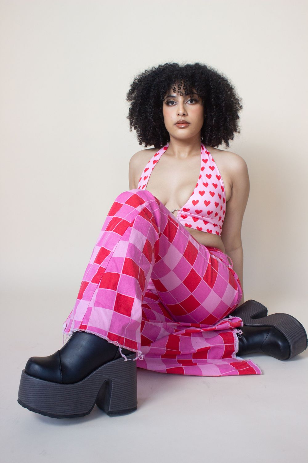Fashion model in pink checkered dress and platform boots poses against neutral background.