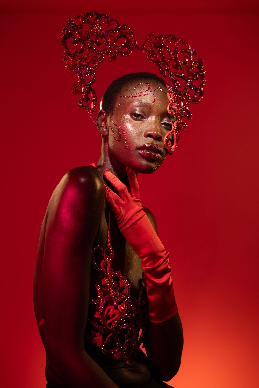 Dramatic artistic beauty portrait with red gloves and crystal hair accessories against red bright background.