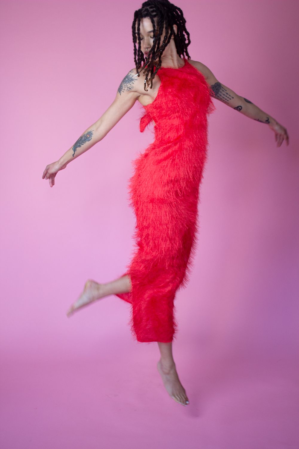 Dancing figure in vibrant red furry dress against pink background.